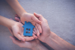 two pair of hands holding a small house in the middle